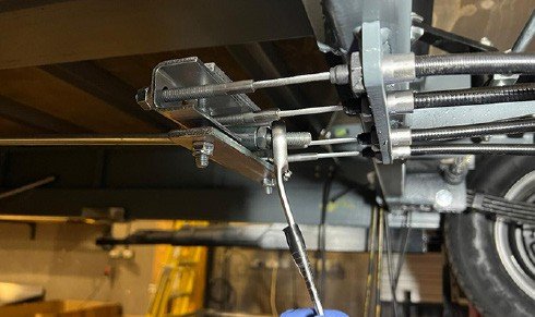 Fig. 66 — Under-chassis view of the brake rod and cable compensator assembly on the Charge Space. The compensator bar (horizontal), brake cables (left and right), M8 adjuster nuts, and brake rod (lower) are all visible. This is the assembly that must be set before the brake setting procedure can begin