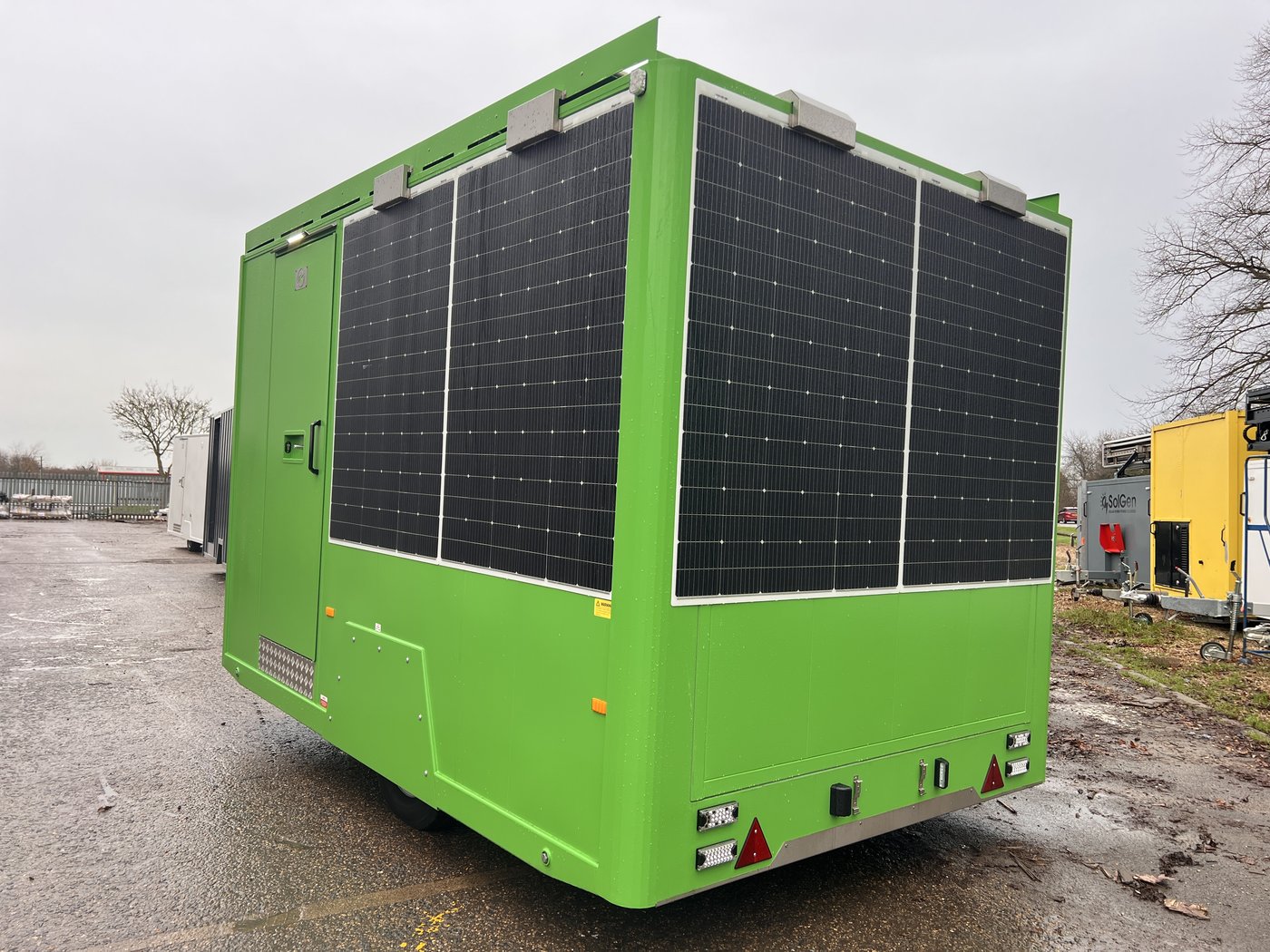 Fig. 4 — Rear left view on road wheels, showing the full six-panel wall-mounted solar array, red reflectors at the lower corners, and road lighting cluster at the base