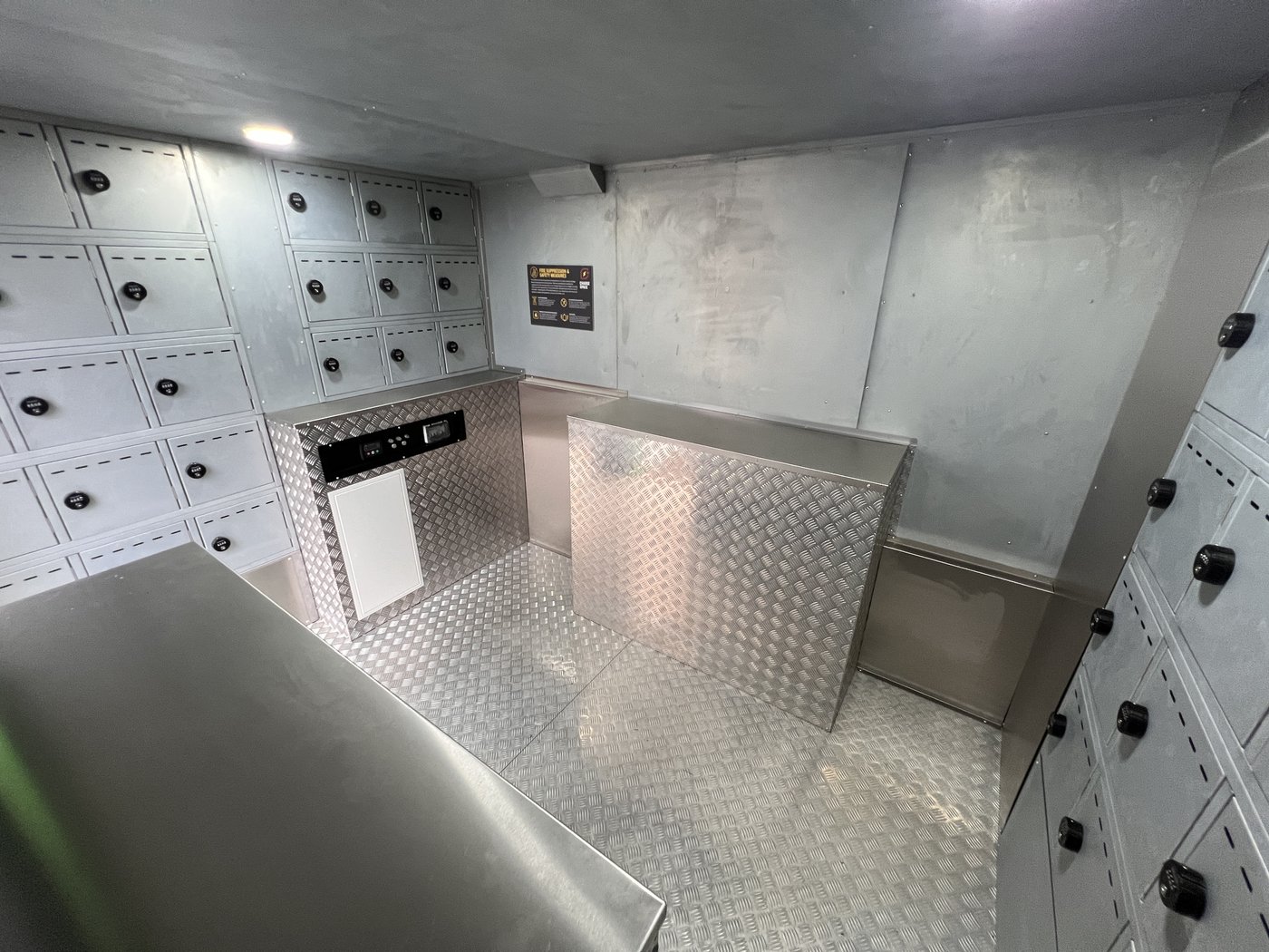 Fig. 50 — Interior from rear showing the central chequerplate counter unit with the SOLARTrack™ display screen (centre), left-hand and right-hand compartment banks, and the circular PIR ceiling light above. The chequerplate work surfaces and stainless steel shelf are visible