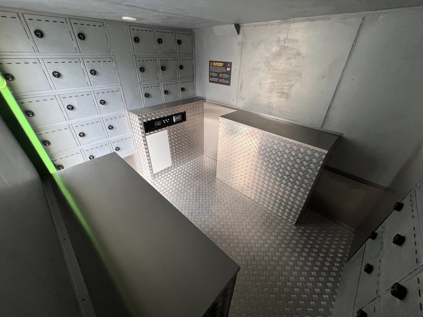 Fig. 14 — High-angle overhead view from the rear left, showing the full interior layout: compartment banks on both walls, the chequerplate counter unit with integrated display screen, and the stainless steel work surfaces