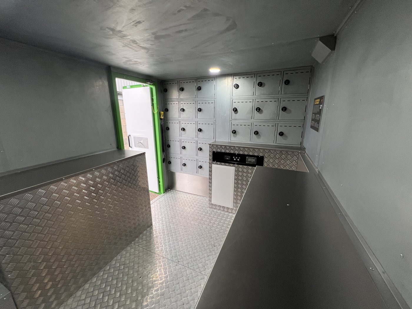 Fig. 11 — Interior overview from the rear right, looking towards the open access door. The central counter unit with display screen is visible centre-left, with compartments on both the right wall and the far wall behind the door